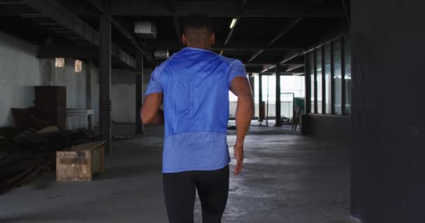 スポーツウェアを着たアフリカ系アメリカ人が空の都市の建物をジョギングしている — ストック動画