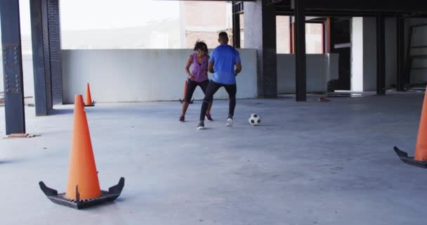 Africano americano homem e mulher jogando futebol em um edifício urbano vazio — Vídeo de Stock