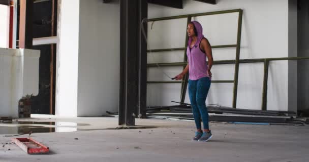 Afričanky americká žena nosí mikinu skákání s lanem v prázdné městské budově — Stock video