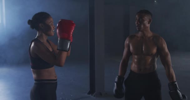 Hombre y mujer afroamericanos usando guantes de boxeo entrenando lanzando puñetazos en habitación vacía — Vídeos de Stock