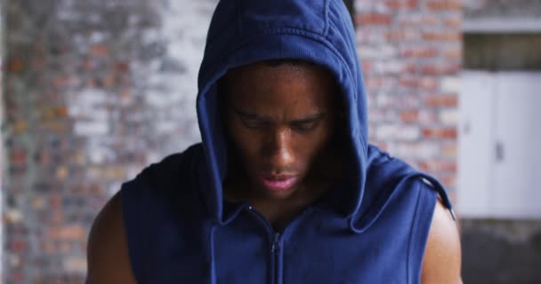 Porträtt av afrikansk amerikansk man bär huvtröja svettas efter träning tittar på kameran i urban b — Stockvideo