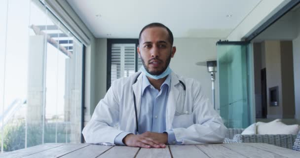 Mixed race male doctor wearing face mask talking during video call — Stock Video