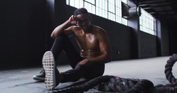 Homem afro-americano sem camisa descansando depois de lutar contra cordas em um prédio urbano vazio — Vídeo de Stock