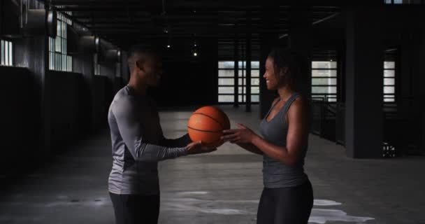 Αφροαμερικάνος άντρας και γυναίκα στέκονται σε ένα άδειο κτίριο παίζοντας μπάσκετ. — Αρχείο Βίντεο