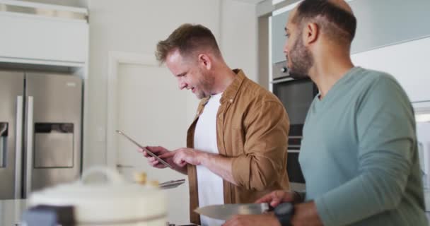 Multi ethnique gay mâle couple préparation de la nourriture dans la cuisine un en utilisant la tablette — Video