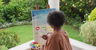 Evin verandasında dikilen yaşlı Afro-Amerikan kadın resminin arkası.