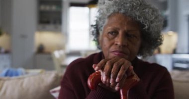 Düşünceli son sınıf Afrikalı Amerikalı kadın elinde bastonla evdeki kanepede oturuyor.