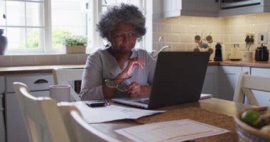 Kıdemli Afro-Amerikan kadın dizüstü bilgisayar kullanıyor ve evdeki mali hesapları hesaplıyor.