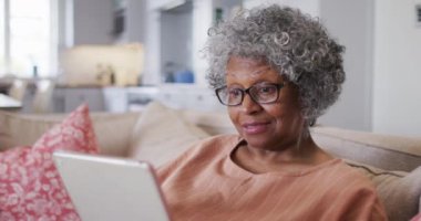 Kıdemli Afro-Amerikan kadın ho 'da kanepede otururken dijital tablette görüntülü konuşma yapıyor.