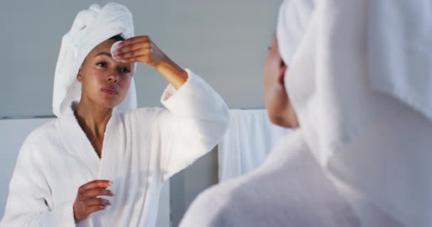 Afričanky americká žena v županu čištění její tvář s bavlněnou podložkou při pohledu do zrcadla na bathro — Stock video