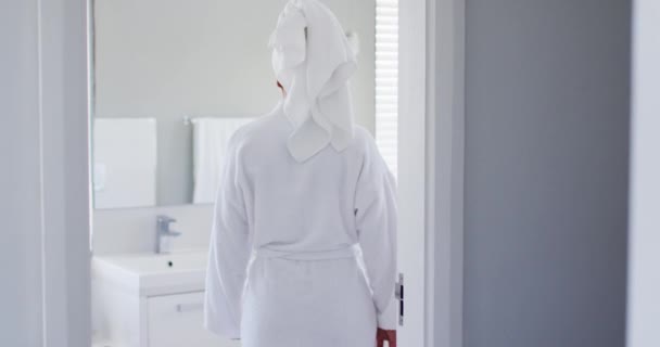 Afrikaans amerikaanse vrouw in badjas aanraken van haar gezicht kijken in de spiegel op badkamer — Stockvideo