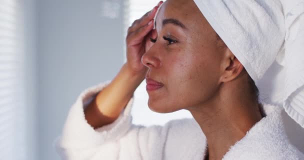 Zblízka africké americké ženy v županu čištění její obličej s bavlněnou podložkou v koupelně — Stock video