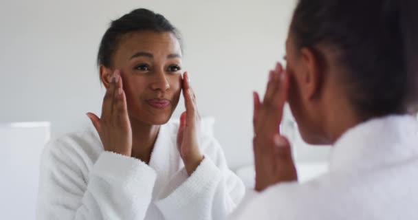 Afroamericano donna in accappatoio toccare il suo volto guardando nello specchio a bagno — Video Stock