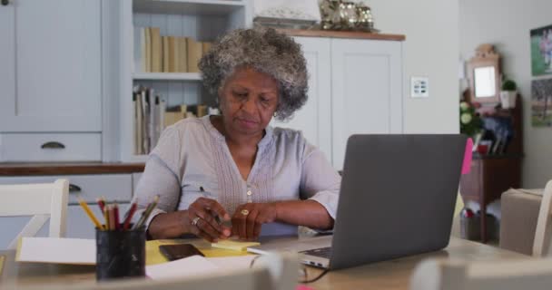 Idősebb afro-amerikai nő jegyzetel a laptopján otthon. — Stock videók