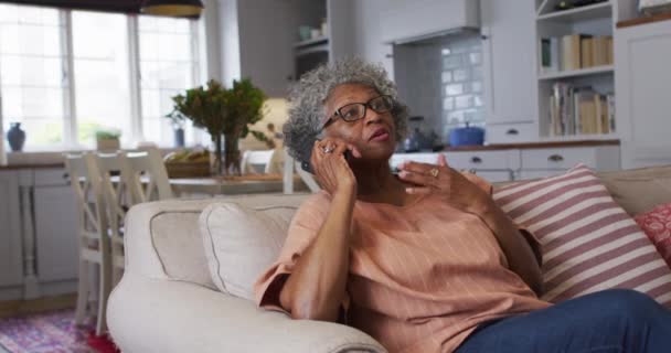 Starsza Afroamerykanka rozmawia na smartfonie siedząc na kanapie w domu — Wideo stockowe