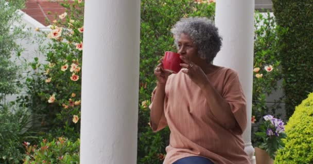 Senior afrikanisch-amerikanische Frau Kaffee trinken, während sie auf der Veranda des Hauses sitzt — Stockvideo