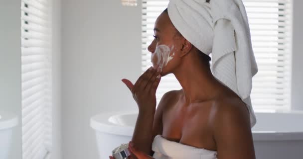 African american woman applying face mask looking in the mirror at bathroom — Stock Video