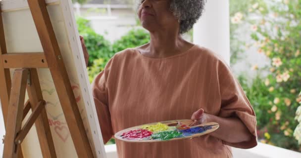 Mujer afroamericana mayor pintando mientras está de pie en el porche de la casa — Vídeos de Stock