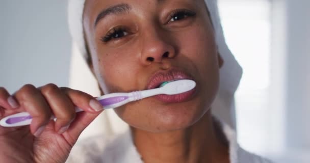 Retrato de mulher afro-americana de roupão escovando os dentes no banheiro — Vídeo de Stock