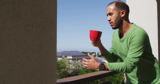 Смешанный гонщик пьет кофе на балконе на солнце — стоковое видео