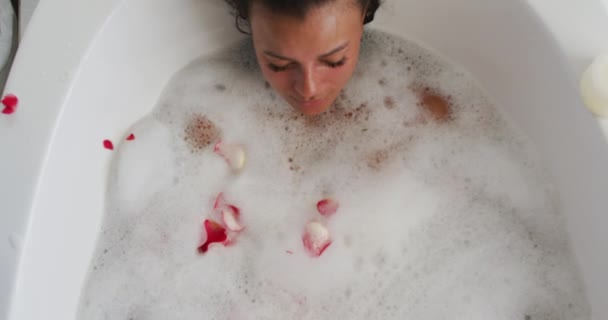 Pétalos de rosa cayendo sobre la mujer afroamericana relajarse en la bañera en el baño en casa — Vídeos de Stock