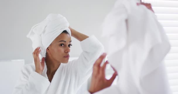 Afro americano donna in accappatoio toccare il suo testa guardando in il specchio a bagno — Video Stock