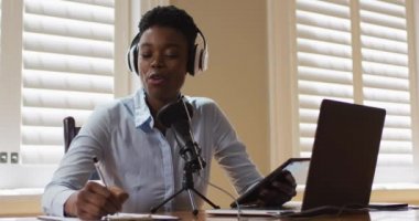 Kulaklık takan Afrikalı Amerikalı kadın not alıyor ve evde şarkı söylüyor.