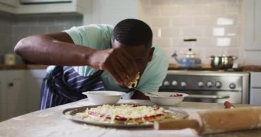 Afro-Amerikalı adam mutfakta pizza yapıyor rendelenmiş peynir serpiyor.