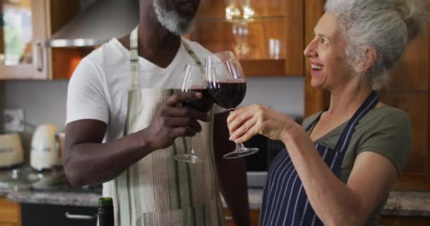 Smíšené závod senior pár připíjení a pití vína společně v kuchyni doma — Stock video