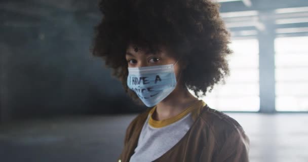 Retrato de mulher afro-americana usando máscara facial de protesto na garagem vazia — Vídeo de Stock