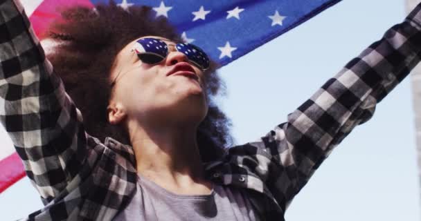 Afroamerykanka w okularach przeciwsłonecznych trzymająca amerykańską flagę w powietrzu — Wideo stockowe