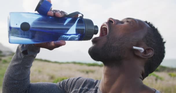 Africano americano homem água potável de garrafa enquanto caminhando nas montanhas — Vídeo de Stock