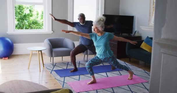 Pareja mayor de raza mixta realizando ejercicio juntos en la sala de estar en casa — Vídeos de Stock
