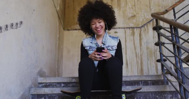 Африканская американка носит наушники, слушая музыку, сидя на лестнице — стоковое видео