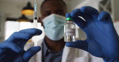 Yüzü maskeli Afrikalı Amerikalı doktor elinde kovid 19 aşısı ve şırınga tutuyordu.