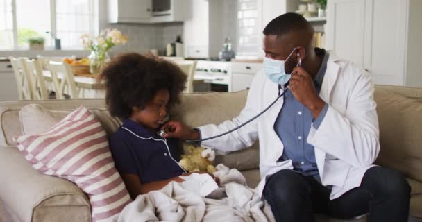Afrika Amerika dokter mengenakan masker wajah menggunakan stetoskop untuk mengobati seorang gadis sakit di rumah — Stok Video