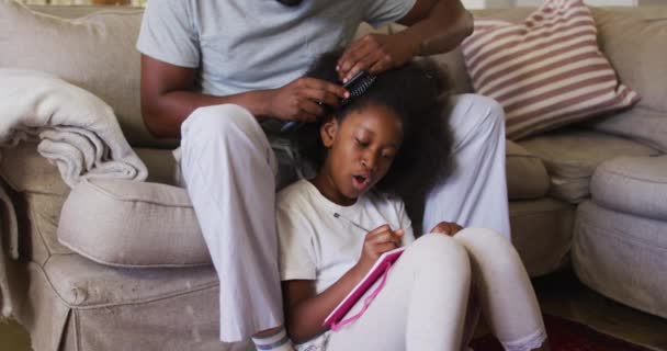 Afro-americano padre cepillando el pelo de sus hijas mientras está sentado en el sofá en casa — Vídeo de stock