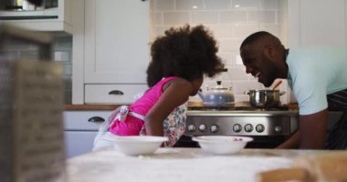 Afrikalı Amerikalı kız ve babası birlikte yemek pişiriyor ve mutfakta beşlik çakıyor. Karantina süresince evde tek başına kalarak eğleniyor..