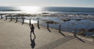 Afrika kökenli Amerikalı kadın sırt çantası takıyor ve deniz kenarında geziniyor.