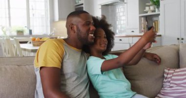 Afrikalı Amerikalı kız ve babası birlikte akıllı telefon kullanıyorlar. Karantina süresince evde tek başına kalmak..