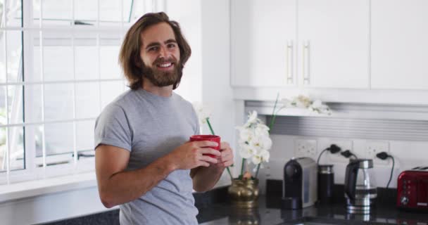 コーヒーカップを持っている白人男性の肖像画や自宅でキッチンで笑顔 隔離されたまま家にいると — ストック動画