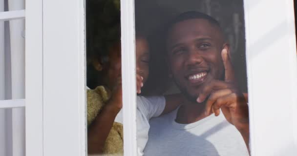 非裔美国人的女儿抱着泰迪熊 和她的父亲一起从窗户往外看 在隔离隔离期间 在家中度过愉快的时光 — 图库视频影像