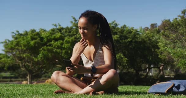 Donna afroamericana seduta sull'erba utilizzando smartphone nel parco — Video Stock