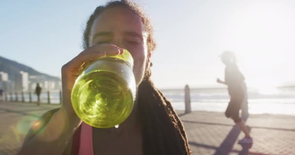 Afroamerykanka w odzieży sportowej pije wodę na promenadzie nad morzem — Wideo stockowe
