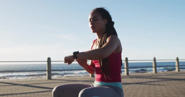 Afričanky americká žena ve sportovním oblečení kontroly smartwatch na promenádě u moře — Stock video