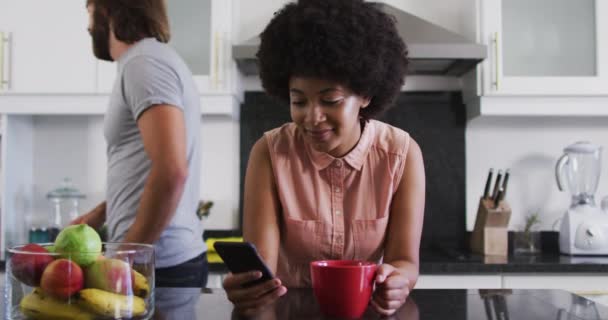 自宅のキッチンでスマホを使ってコーヒーカップを持っているアフリカ系アメリカ人女性 隔離されたまま家にいると — ストック動画