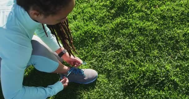 Femme afro-américaine en vêtements de sport attachant ses lacets dans le parc — Video