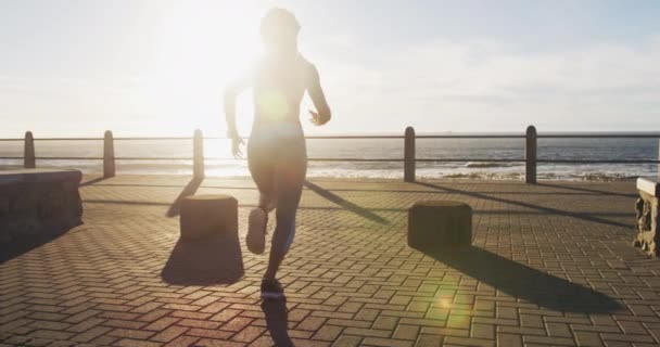 Afrykańska Amerykanka biegnie promenadą nad morzem o zachodzie słońca — Wideo stockowe