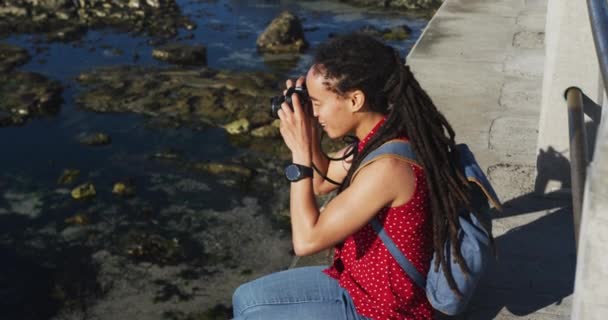 Afroamerikanerin sitzt an der Strandpromenade und fotografiert — Stockvideo