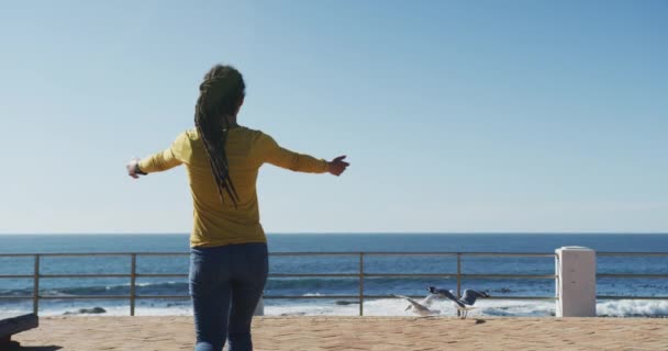 Afrykańska Amerykanka spacerująca z ramionami rozciągniętymi po promenadzie nad morzem — Wideo stockowe